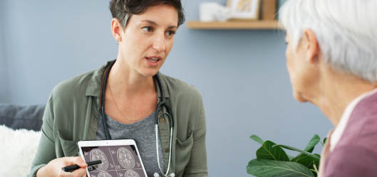 A healthcare professional showing medical scan images on a tablet while speaking with another person in a consultation setting
